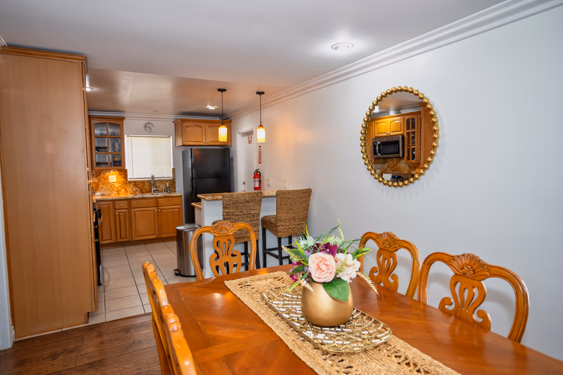 Wood dining table with a floral centerpiece in a dining area beside a kitchen.