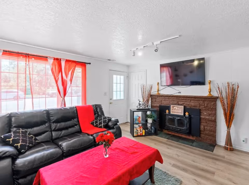 Living room with black leather sofa, red decor, fireplace, and a mounted TV.