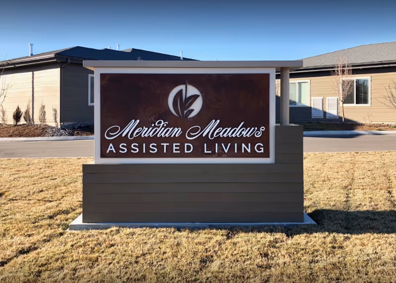 Front view of Meridian Meadows Assisted Living sign with a neighboring building and grassy foreground.