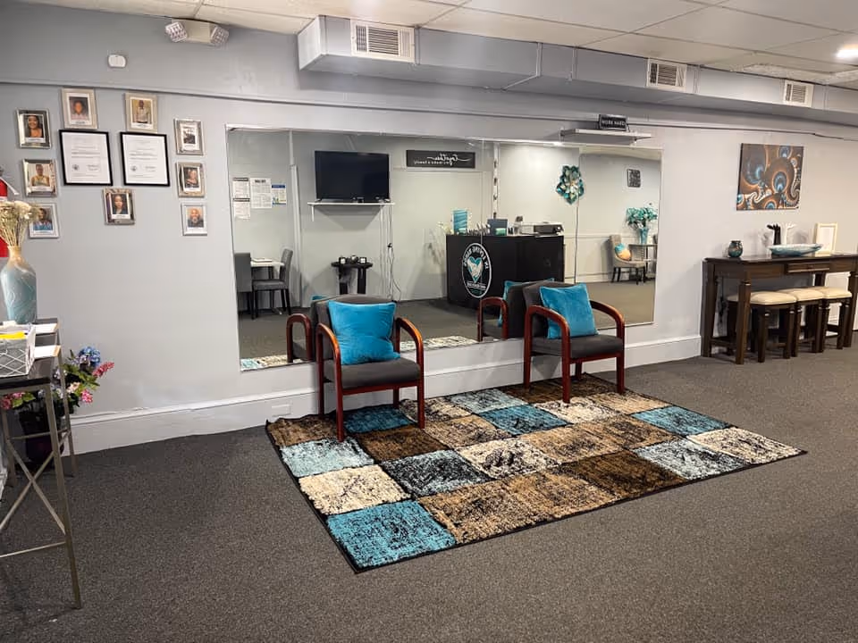Indoor senior living lobby with two teal-pillow chairs, a mirror, reception desk, and rug.