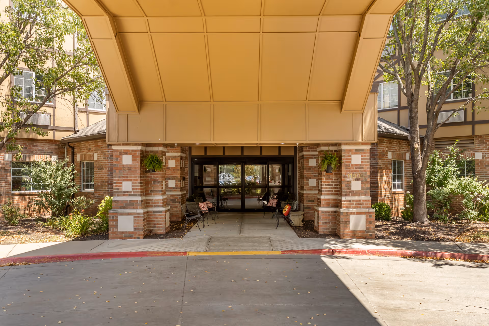 Brick building entrance with a covered drop-off, benches, and surrounding trees.