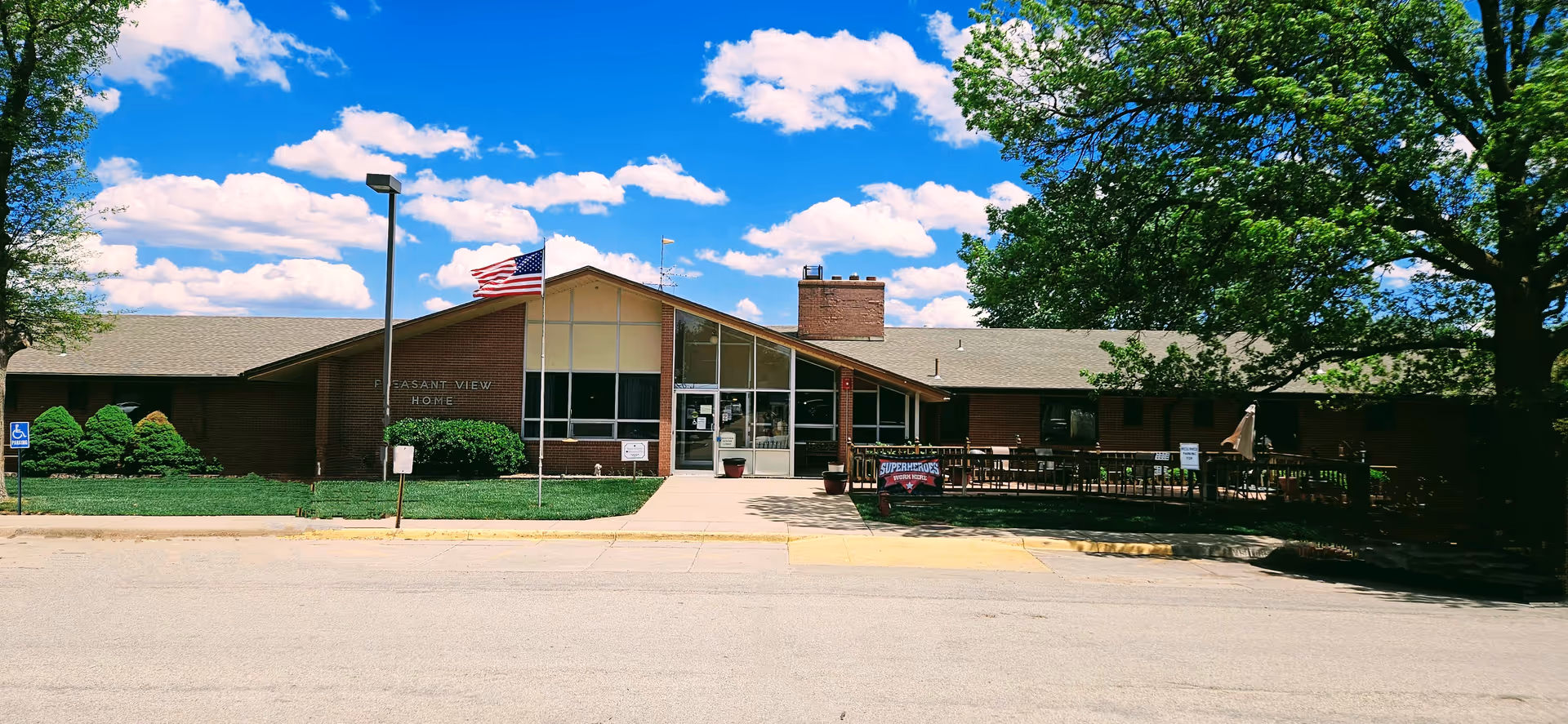 Front view of Pleasant View Home exterior with glass entrance, flag, and surrounding trees.