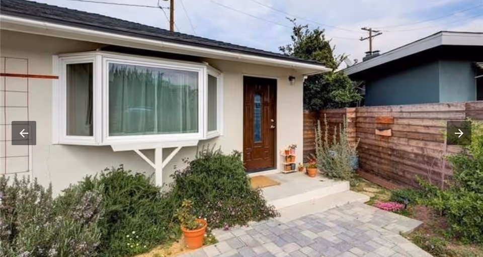 A single-story home entrance with bay window, garden, and a concrete walkway.