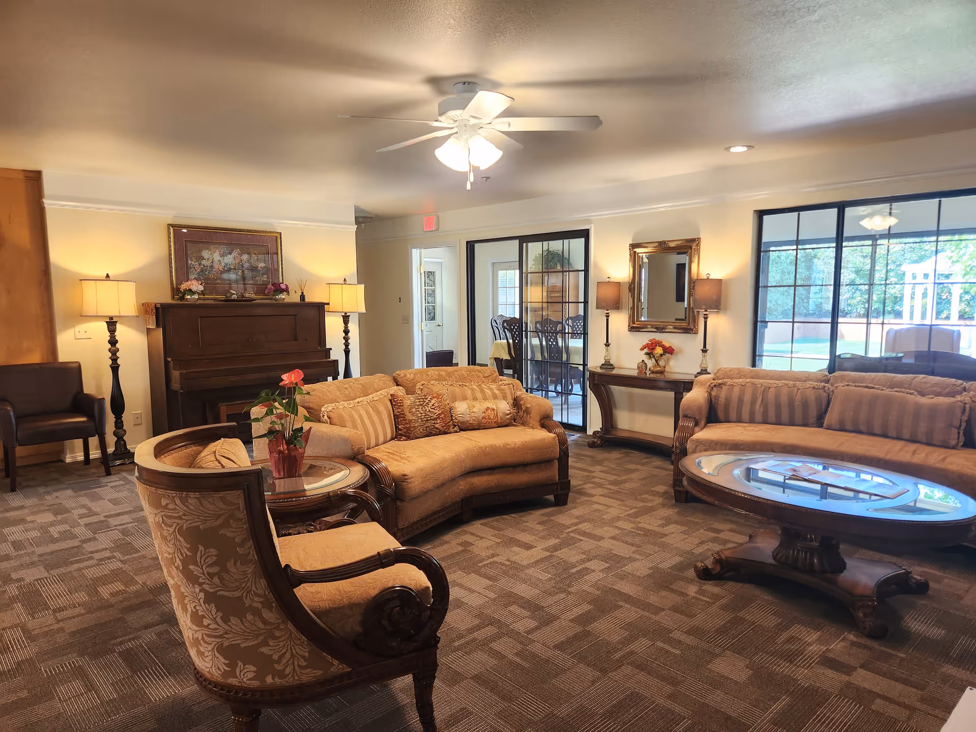 Sunshine House senior living lounge with sofas, a piano, lamps, and glass doors to a patio.