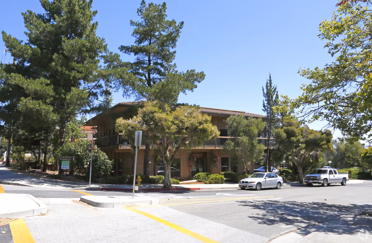 Two-story senior living building with trees, cars, and a street corner.