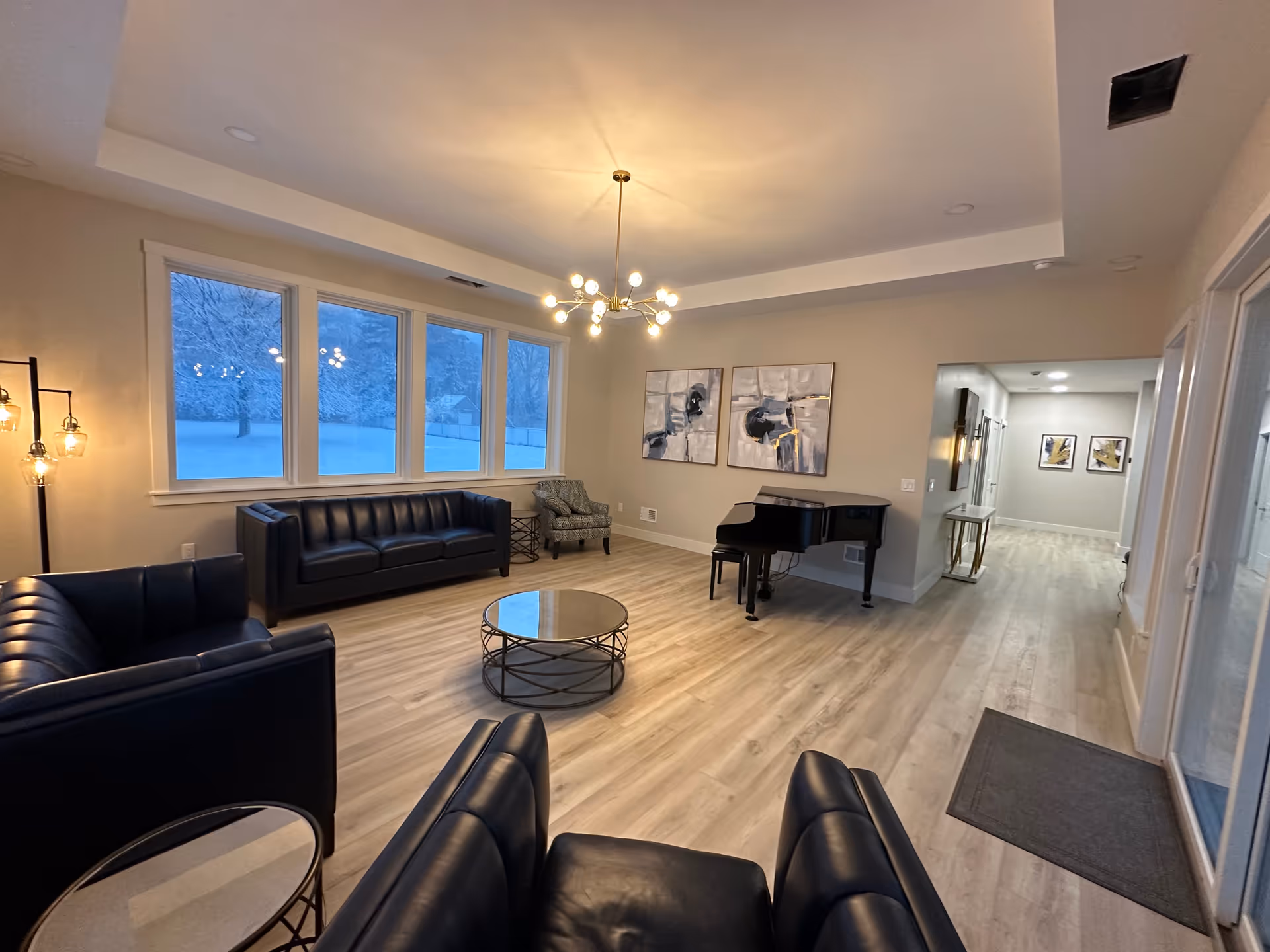 Spacious indoor lounge with black leather sofas, a grand piano, coffee table, and large windows.