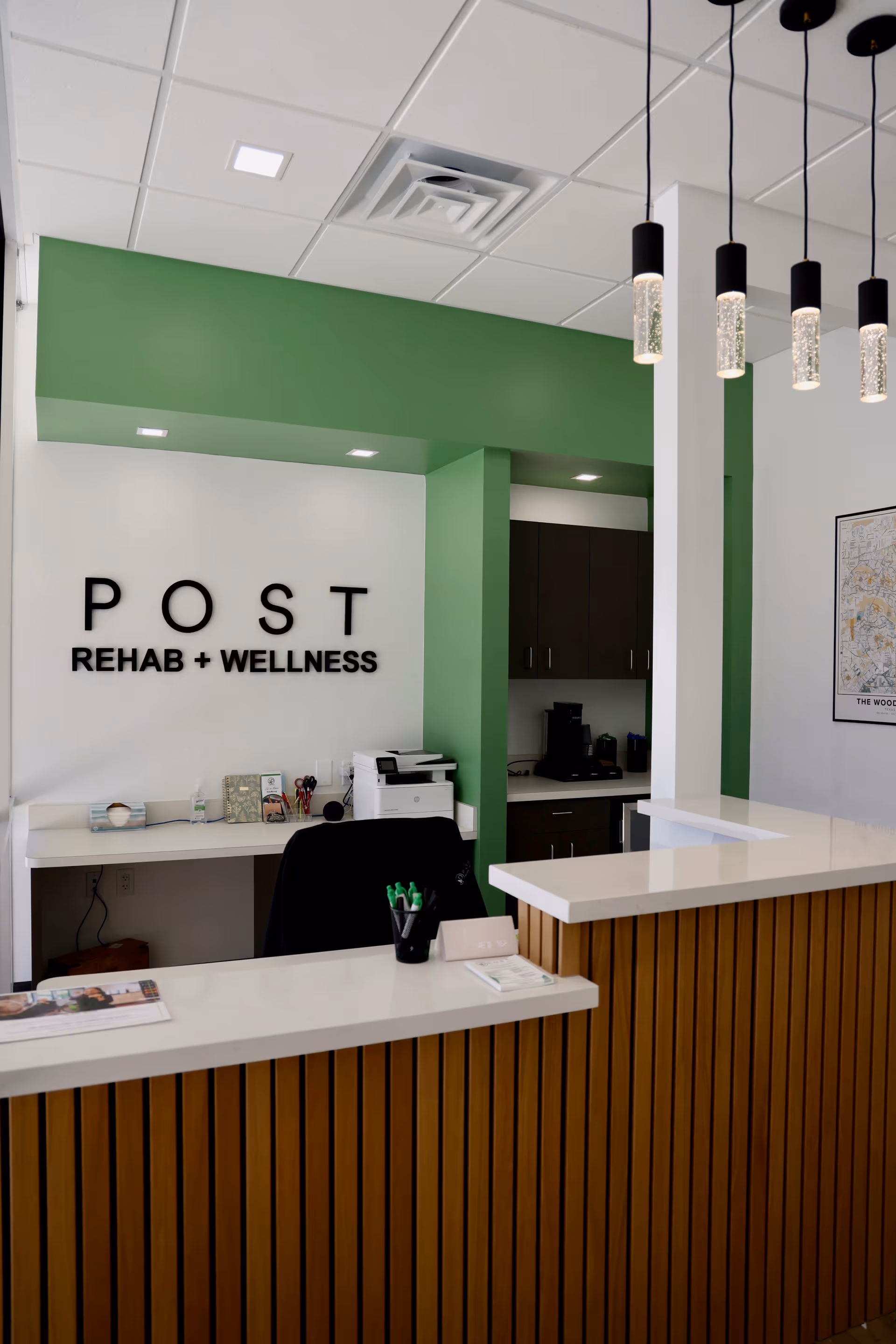 Reception area with front desk, green accent wall, and POST Rehab + Wellness sign.