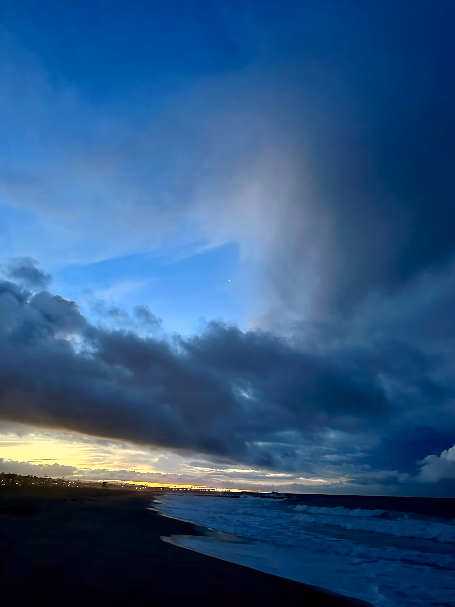 Coastal sunset over the ocean with dark clouds and glowing horizon.