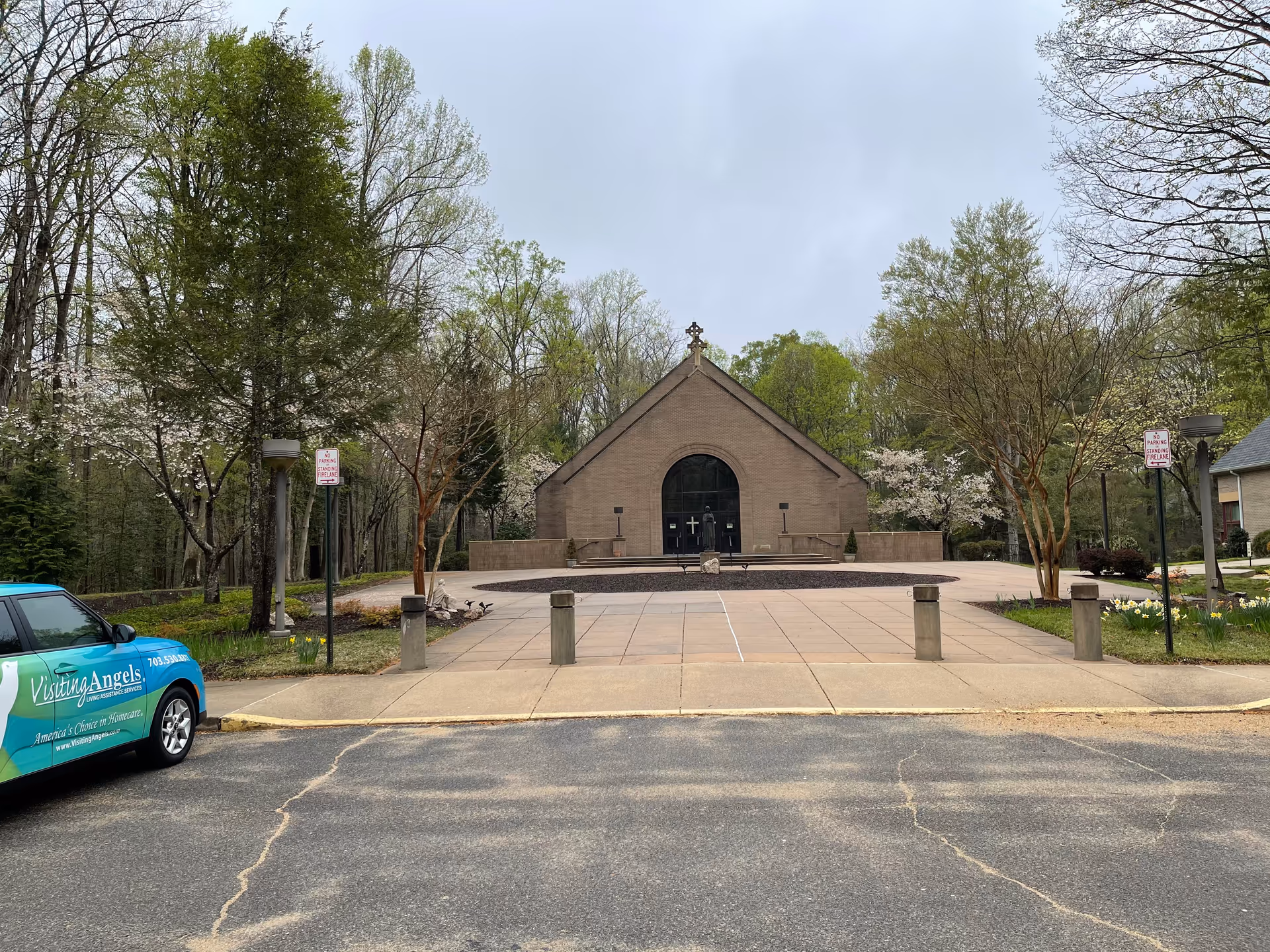 Exterior view of a brick chapel-like building with a circular driveway and a Visiting Angels car.
