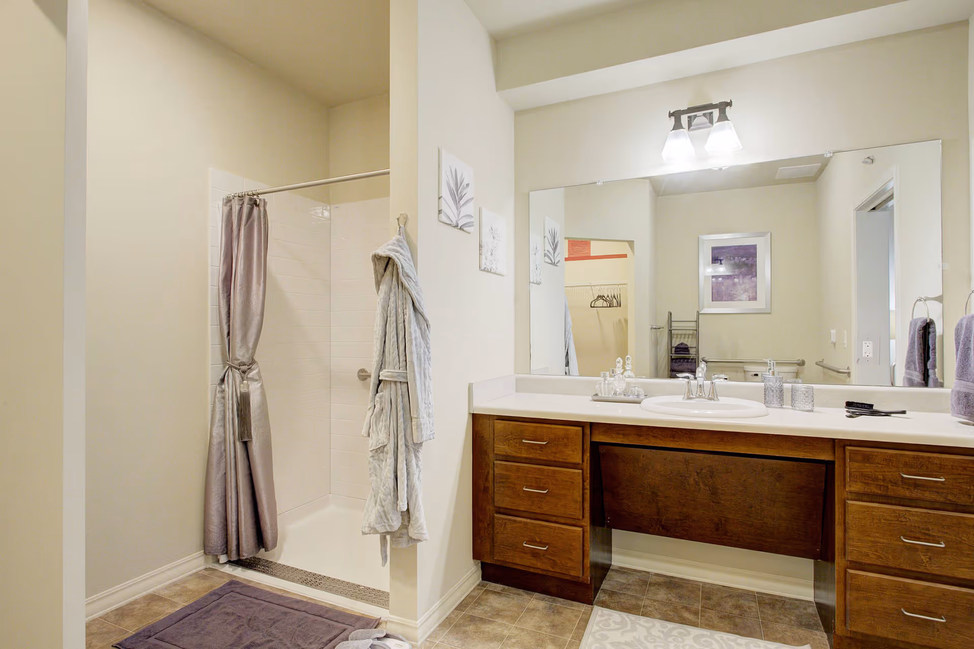 Accessible bathroom with a walk-in shower on the left and a wooden vanity with sink and large mirror on the right.