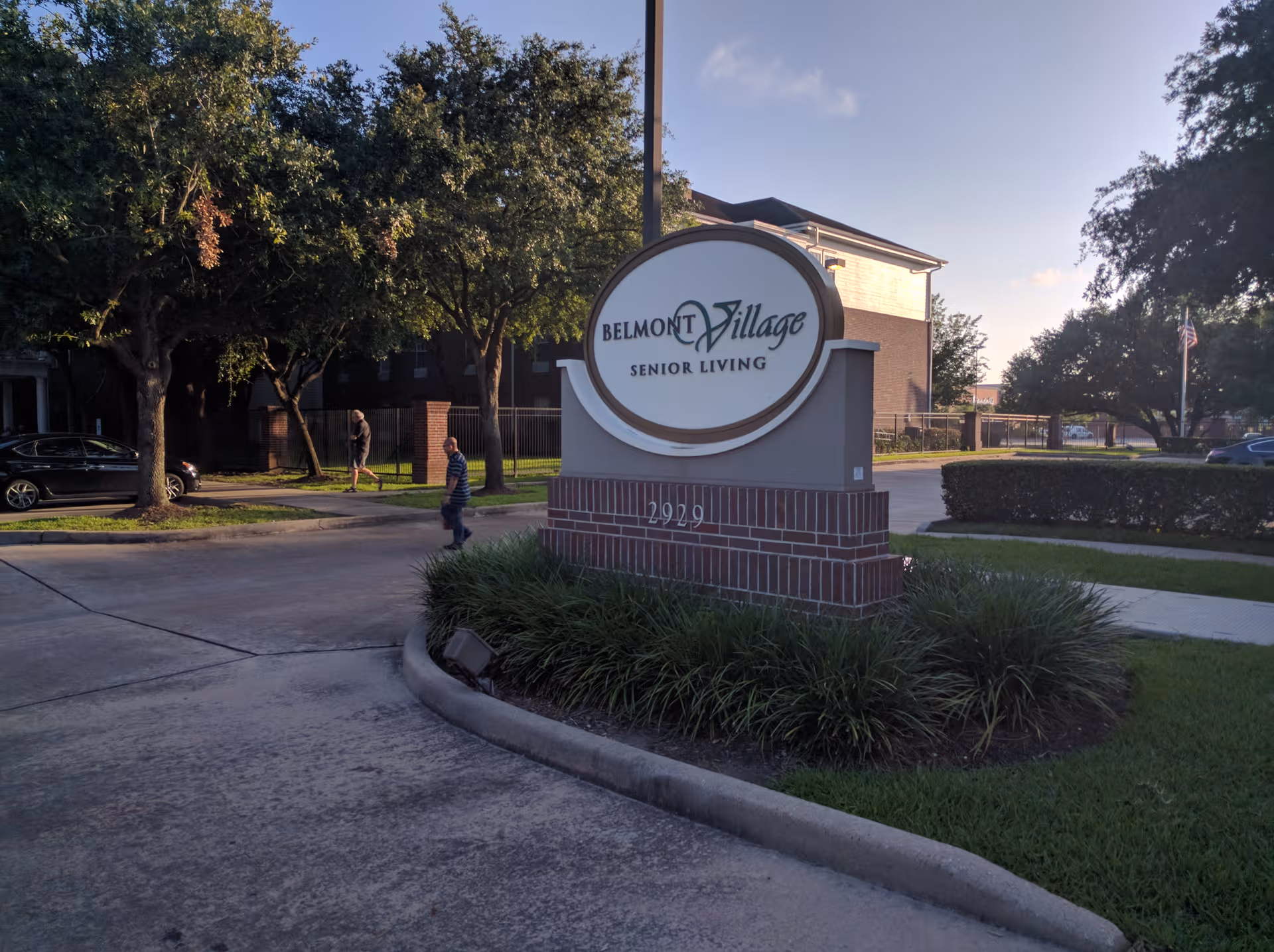 Exterior view of Belmont Village Senior Living sign at the entrance with trees and sidewalk