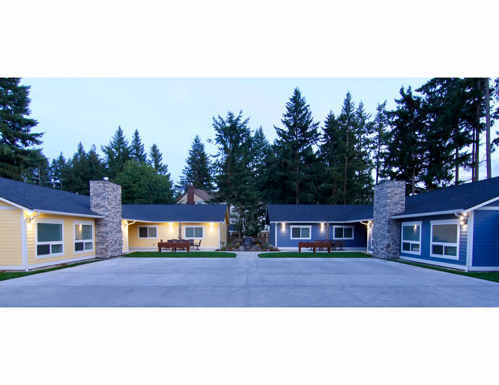 Colorful single-story cottages arranged in a circular courtyard with outdoor seating and trees behind.