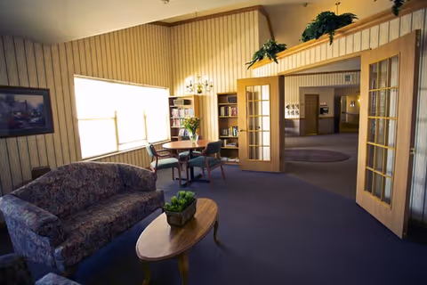 Cozy senior living lounge with sofa, coffee table, chairs, bookshelf, and French doors.