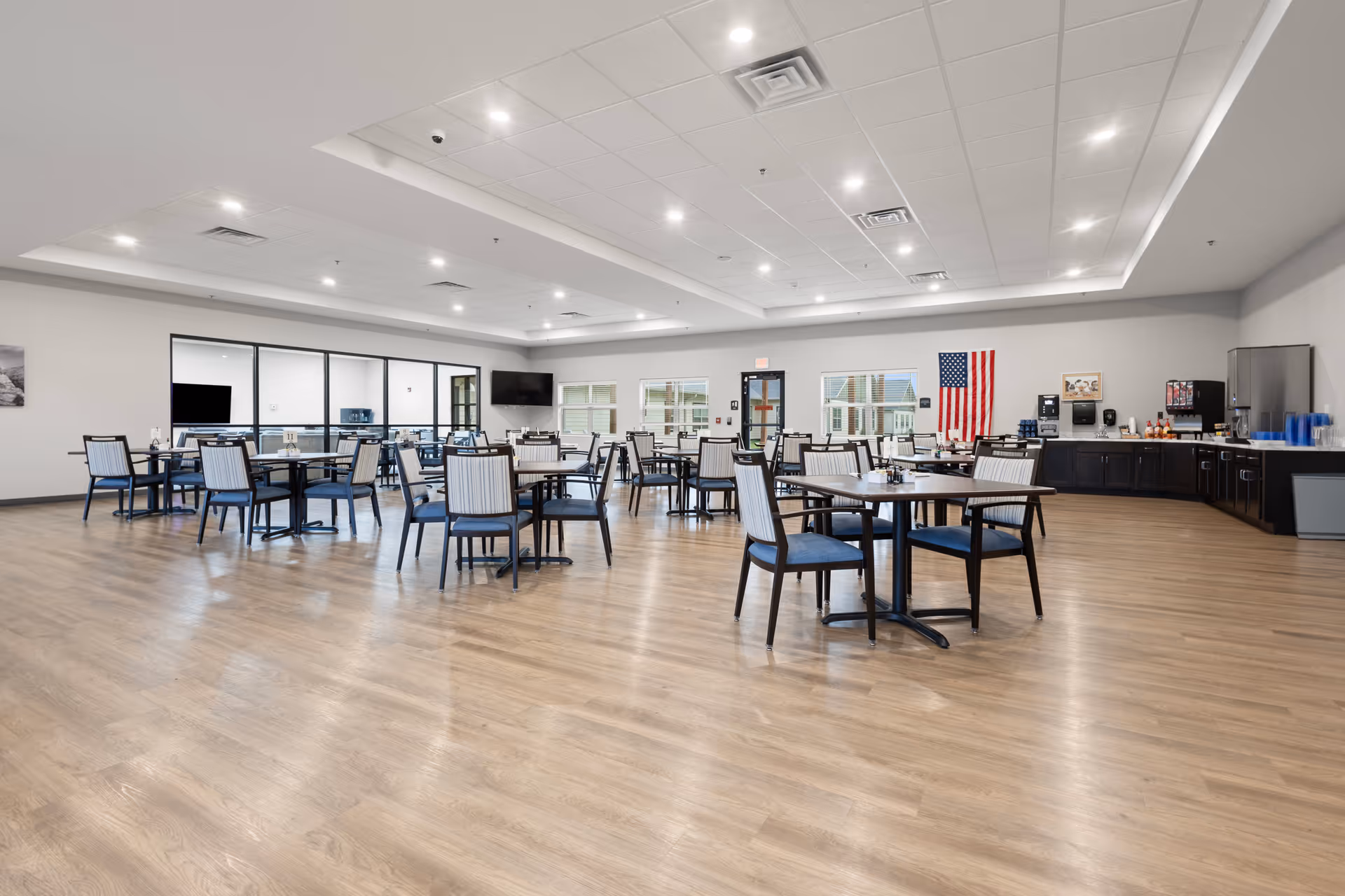 Spacious senior dining hall with round tables, blue chairs, and serving area.