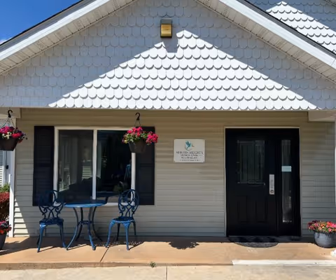 Front exterior of Auburn Heights Senior Care with blue outdoor seating and hanging planters.