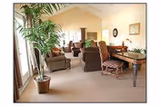 Bright senior living common room with sofas, chairs, and a tall plant.