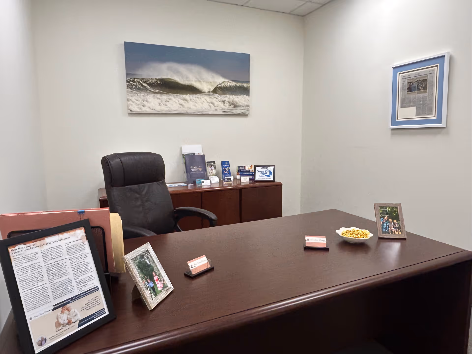 A polished dark wood executive desk in a quiet office with framed photos and ocean art.