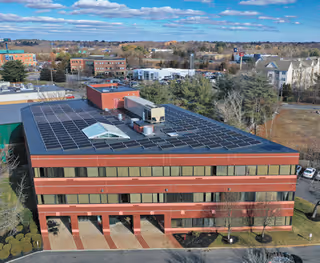A multi-story red-brick building with extensive solar panels on a flat roof.