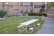 Outdoor courtyard with a white picnic table on a grassy area near a brick building