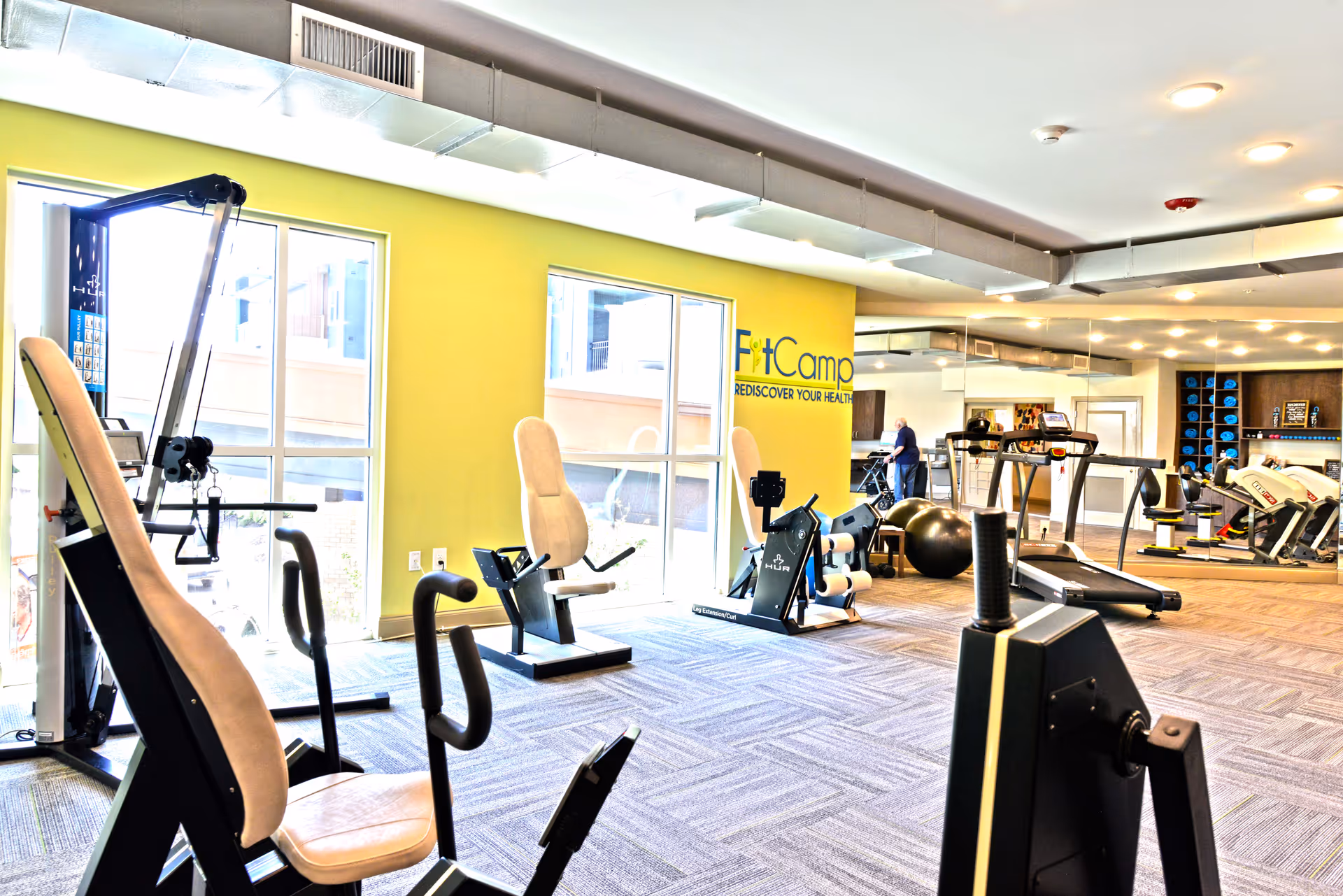 Bright fitness center with treadmills, weight machines, and seating inside a modern senior living facility.