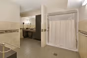Accessible senior living facility bathroom with shower curtain, sink vanity, and grab bars.