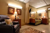 Cozy resident room with leather chair, bed, lamps, artwork, and a patterned rug.