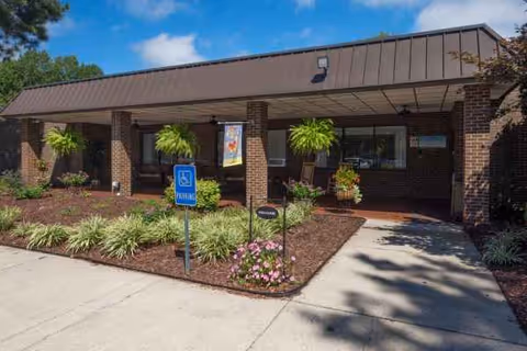 Entrance of White Oak of Burlington, a brick building with a covered walkway and hanging plants.