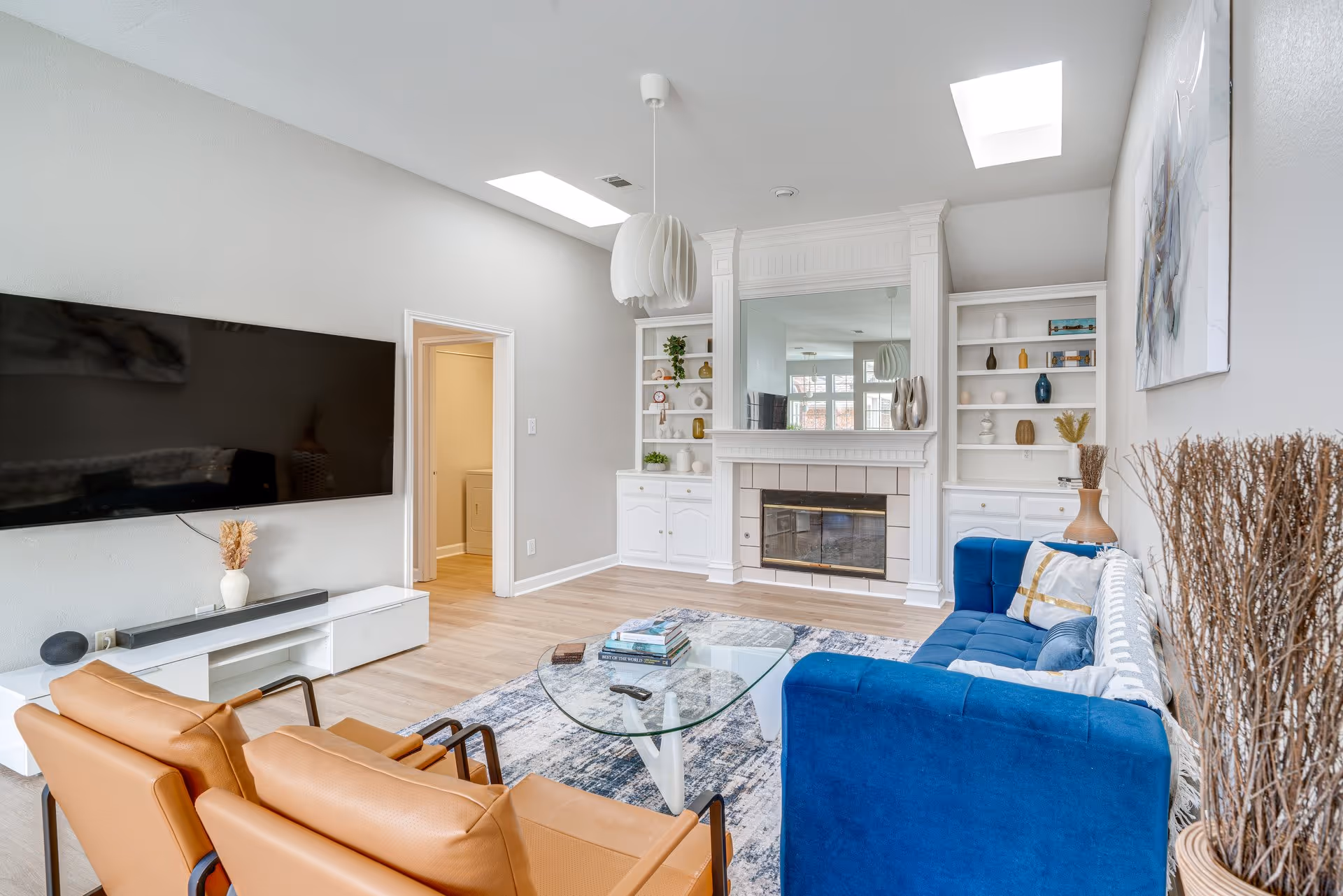 Bright modern living room with blue sofa, tan chairs, fireplace, and wall-mounted TV.