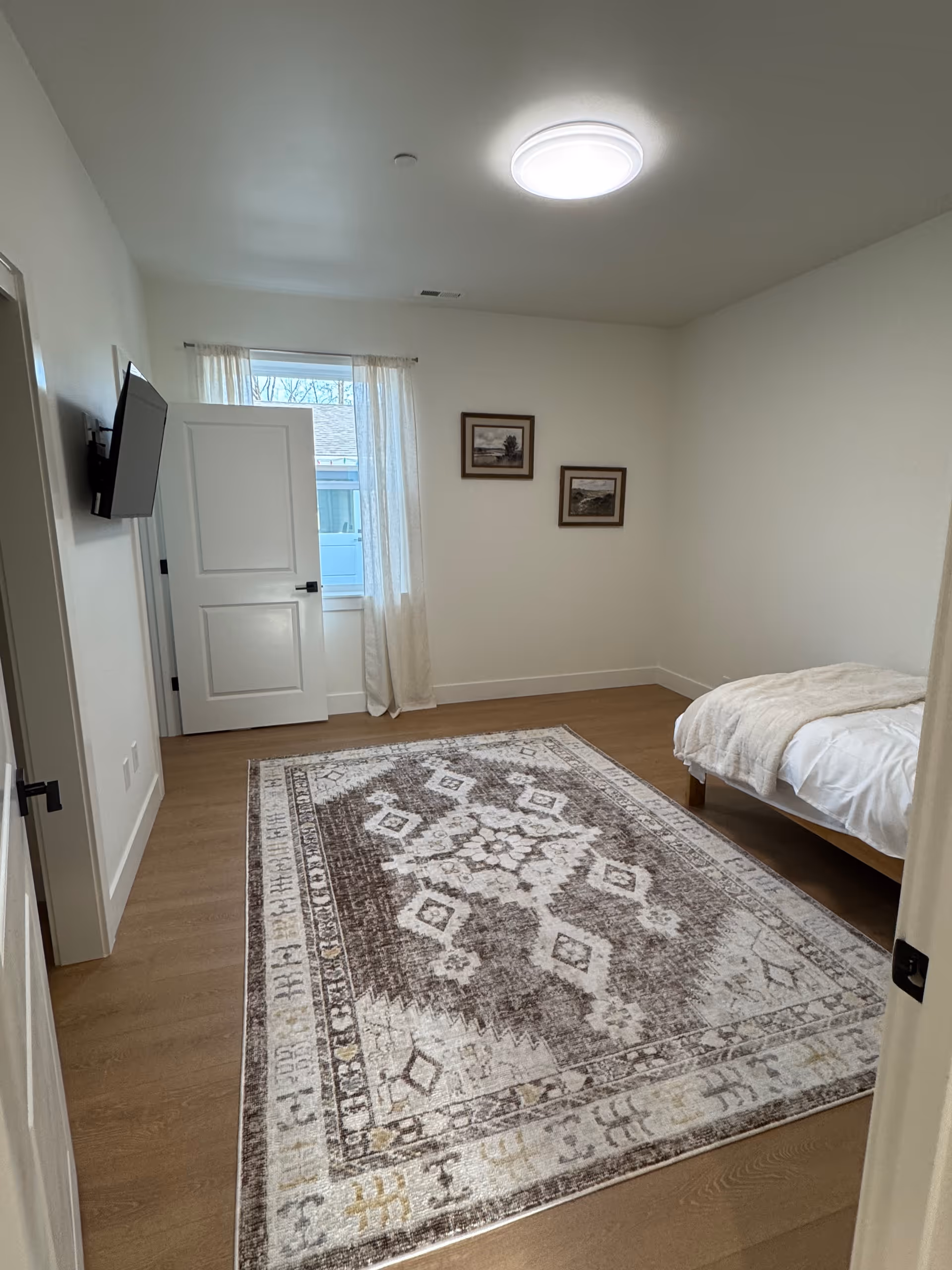 A tidy senior living bedroom with a bed, rug, wall art, and a wall-mounted TV