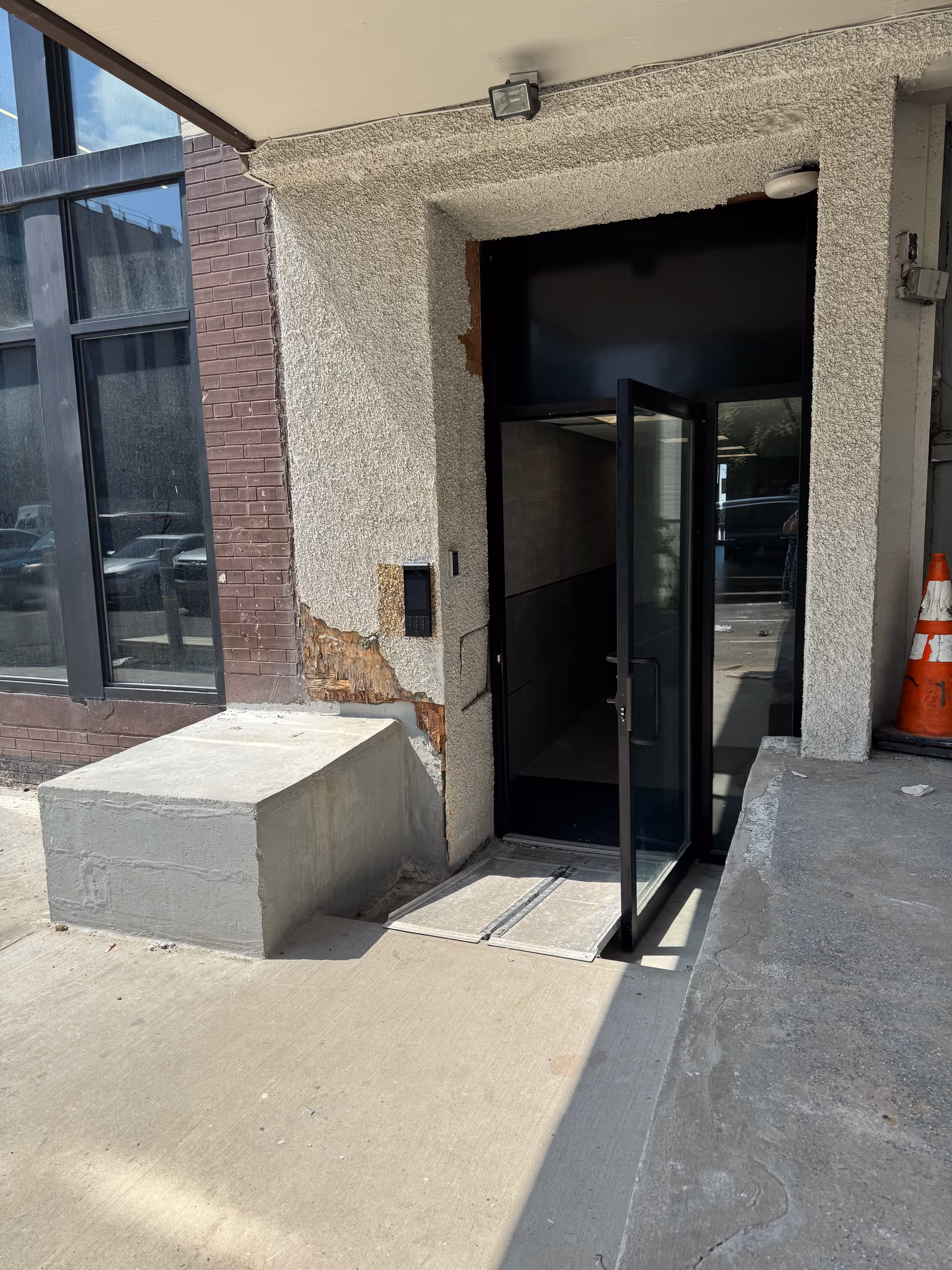 Exterior entrance to a building with a glass door, damaged wall, and concrete ramp.