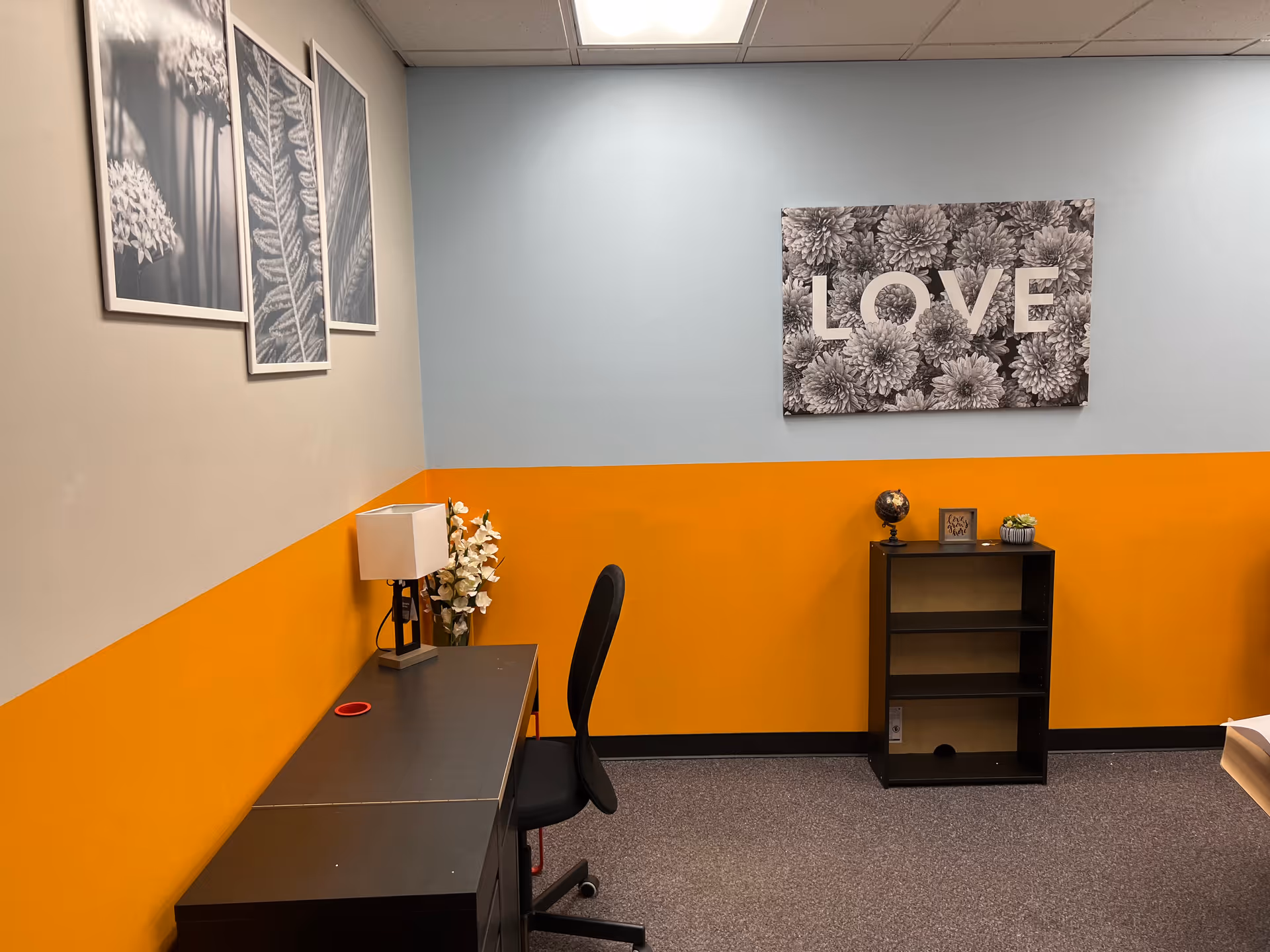 Small office nook with desk, chair, orange-walled lower half, and a large LOVE floral artwork.