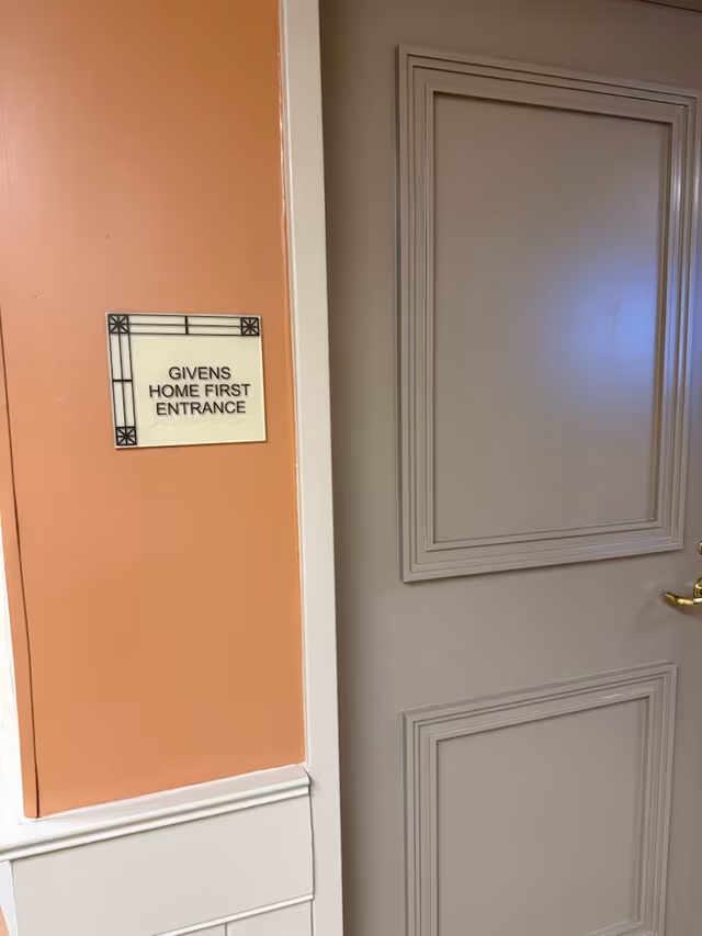 Interior hallway with peach wall, Givens Home First Entrance sign, and a closed door.
