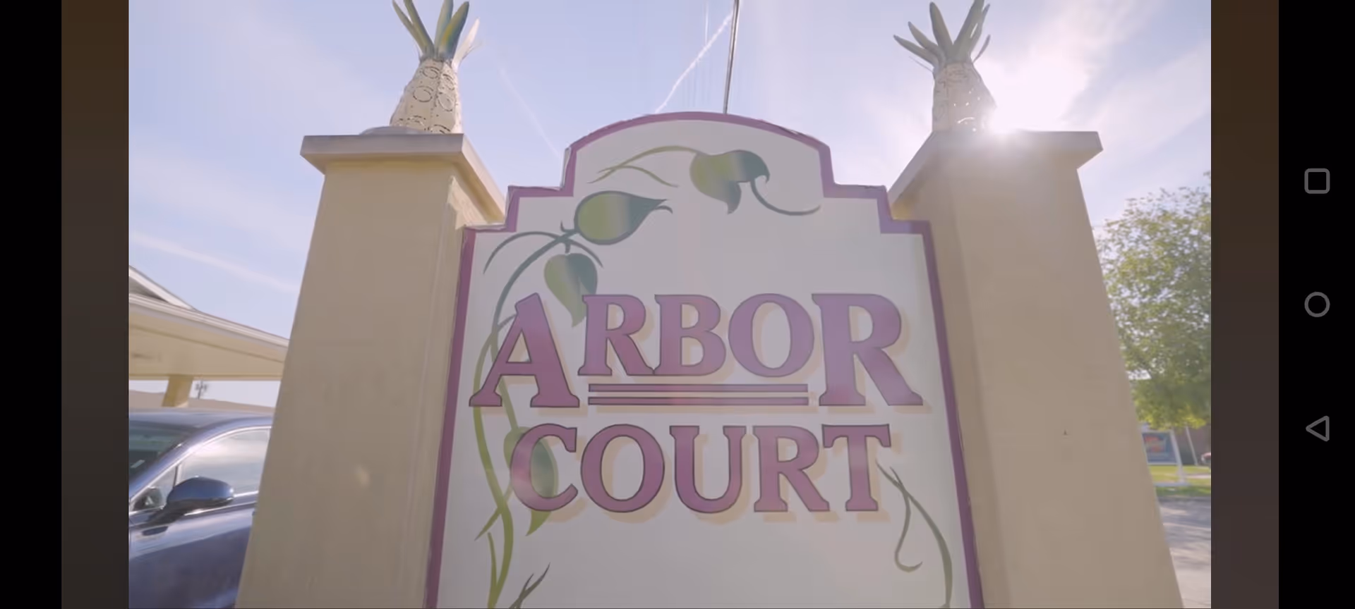 Arbor Court entrance sign between pillars with decorative vines against a sunny sky.