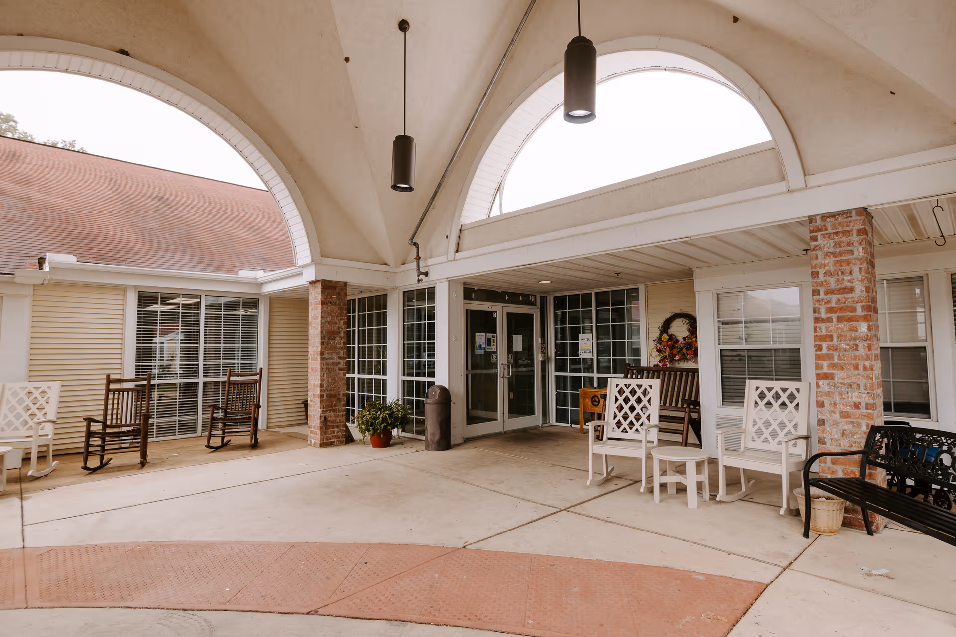 Covered exterior entrance of Belle View Estates with white chairs and brick columns.