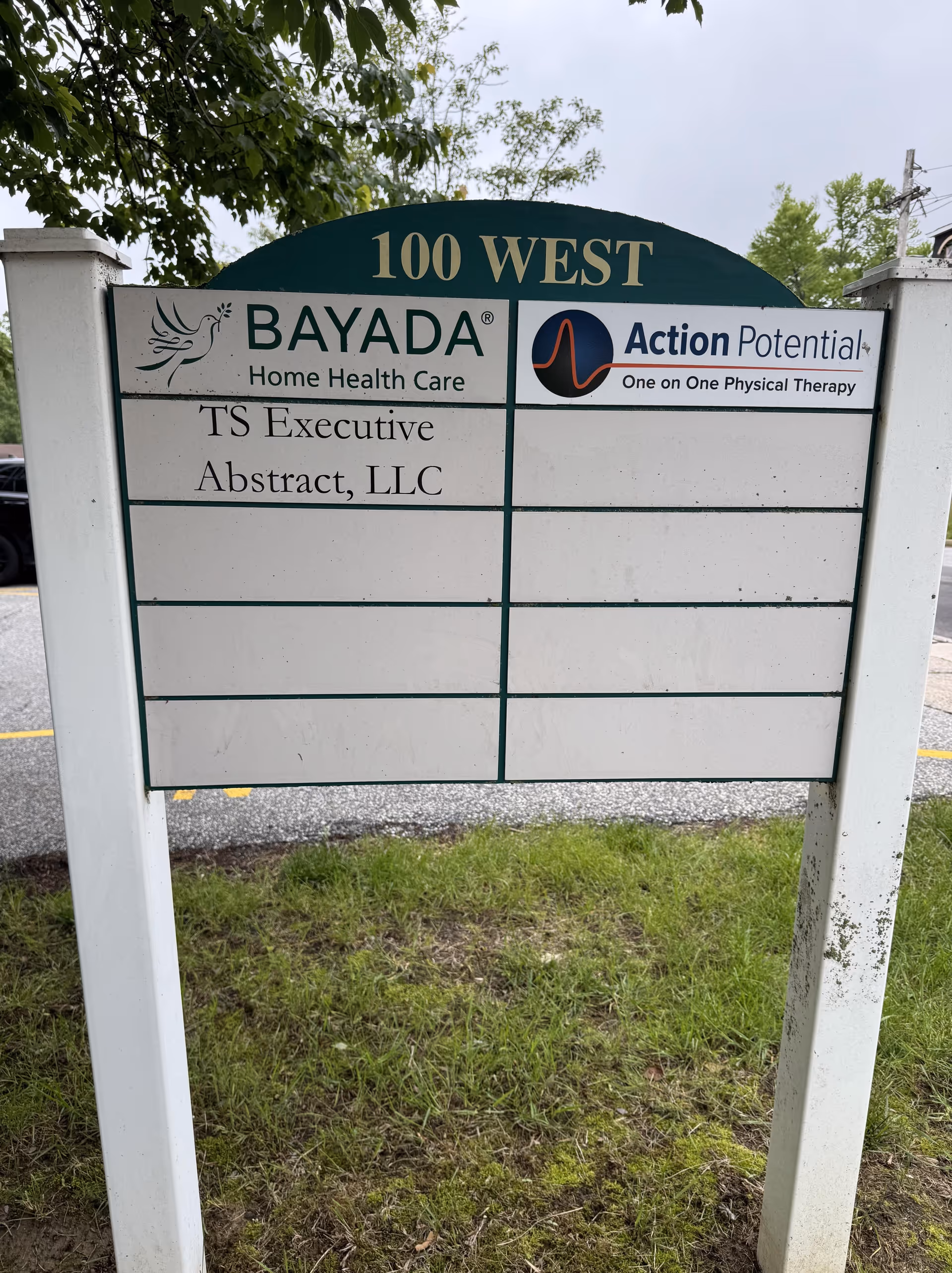 Outdoor signboard at 100 West facility showing BAYADA and partner logos with lawn nearby