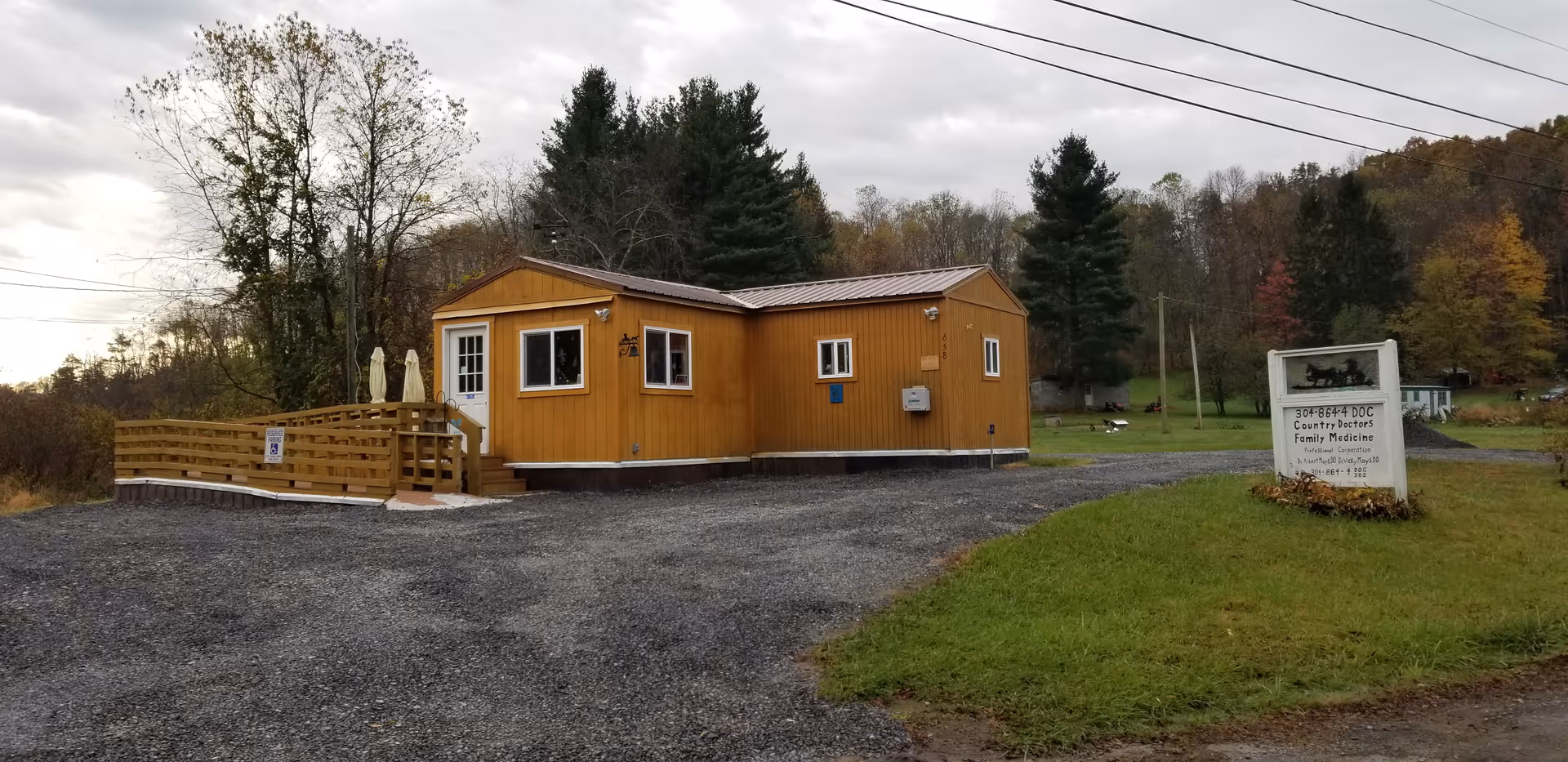 A small yellow wooden clinic building with a ramp, deck, and surrounding lawn.