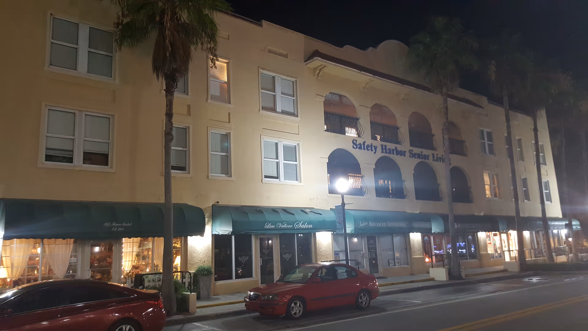 Night view of Safety Harbor Senior Living building with arches and palm trees along the street