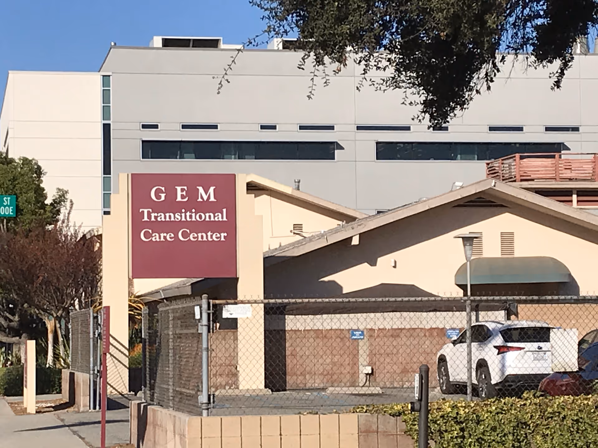 Exterior view of GEM Transitional Care Center with a sign, fence, and parked cars.