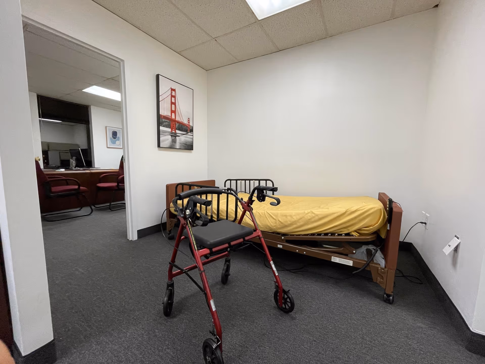 A small clinic room with a hospital bed, yellow bedding, and a walker.