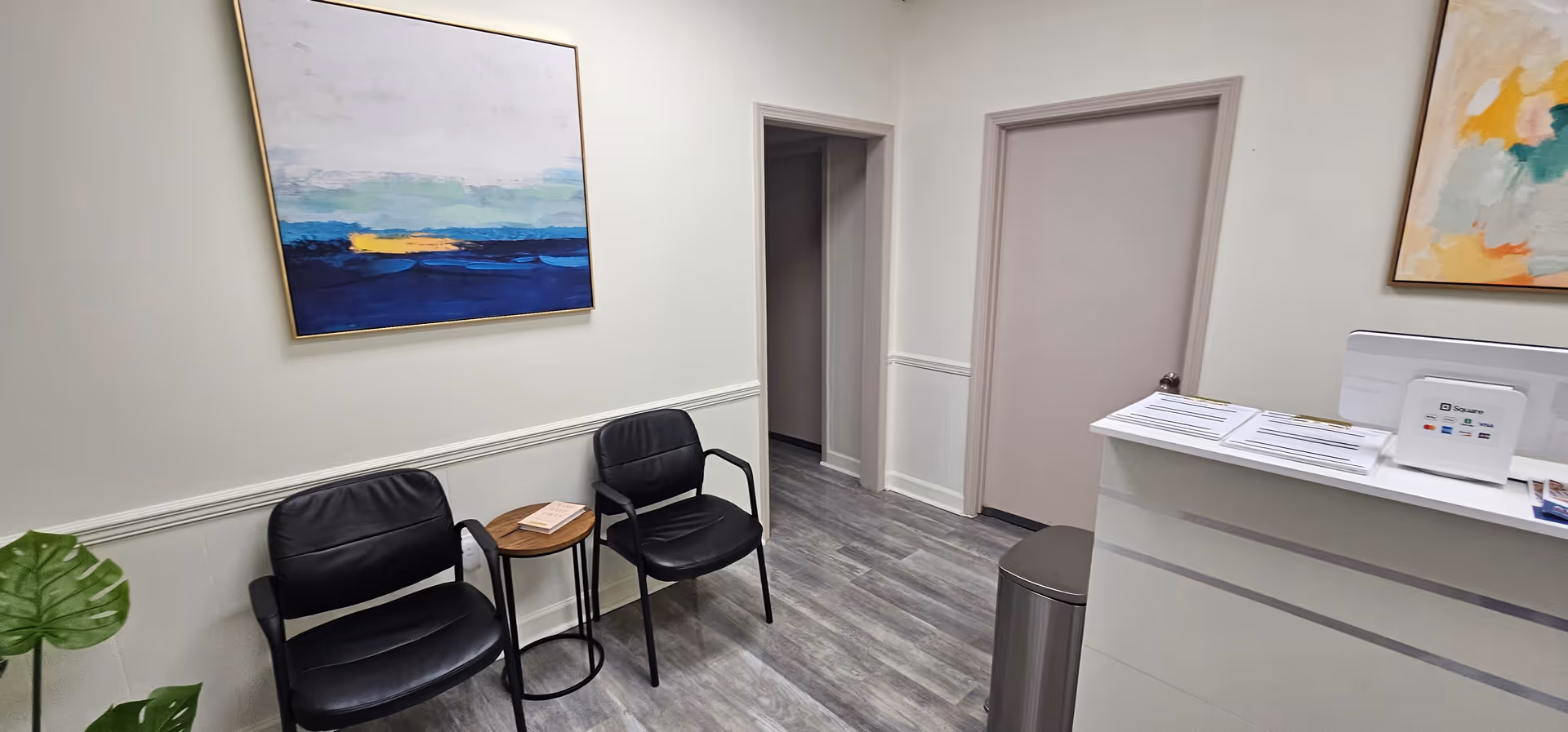 Lobby area with two black chairs, small table, reception desk, and abstract art.