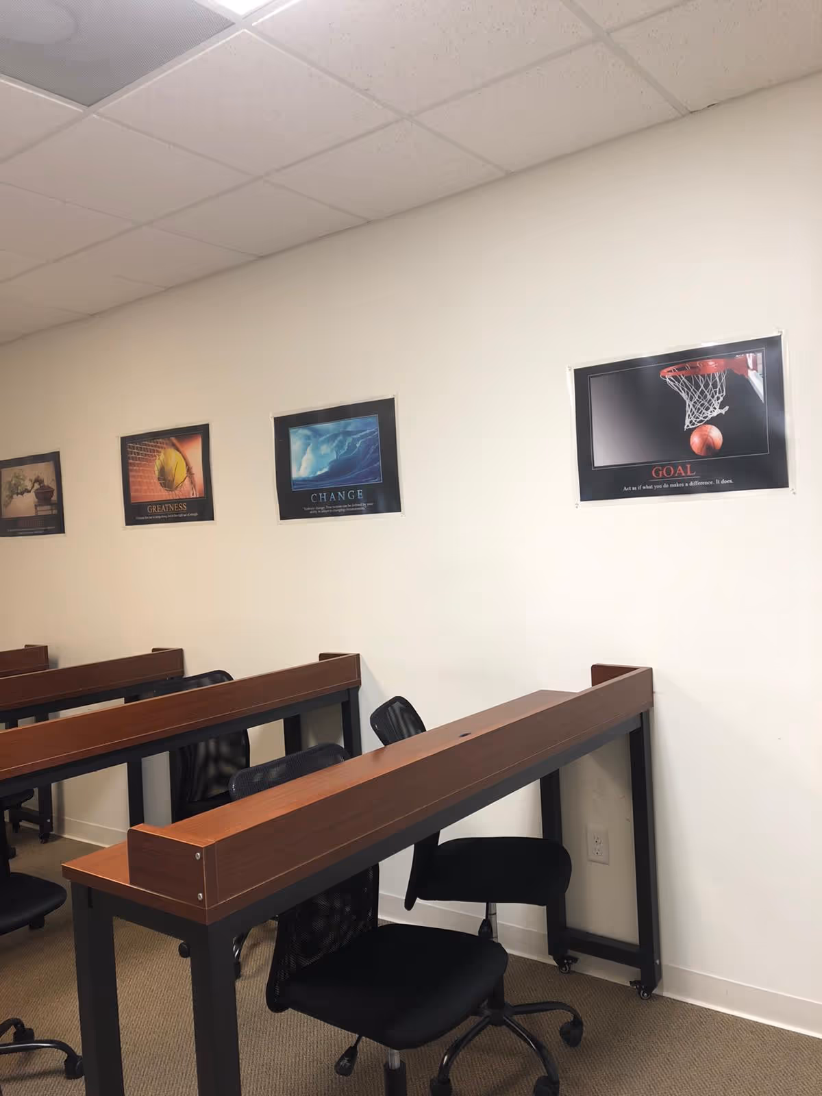 Interior classroom room with long desks, black chairs, and motivational posters along a white wall.