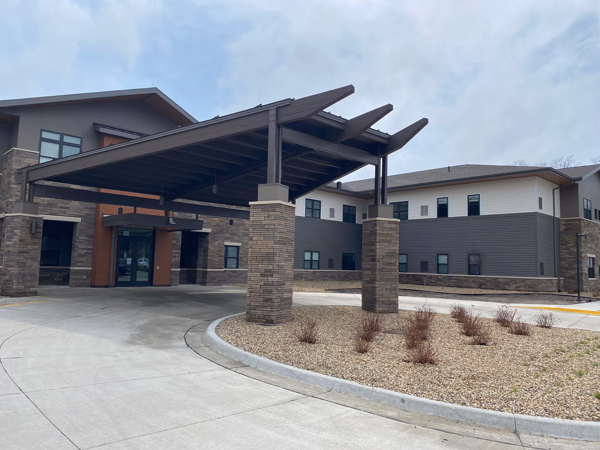 Modern senior living facility exterior with a large covered entrance and stone pillars.