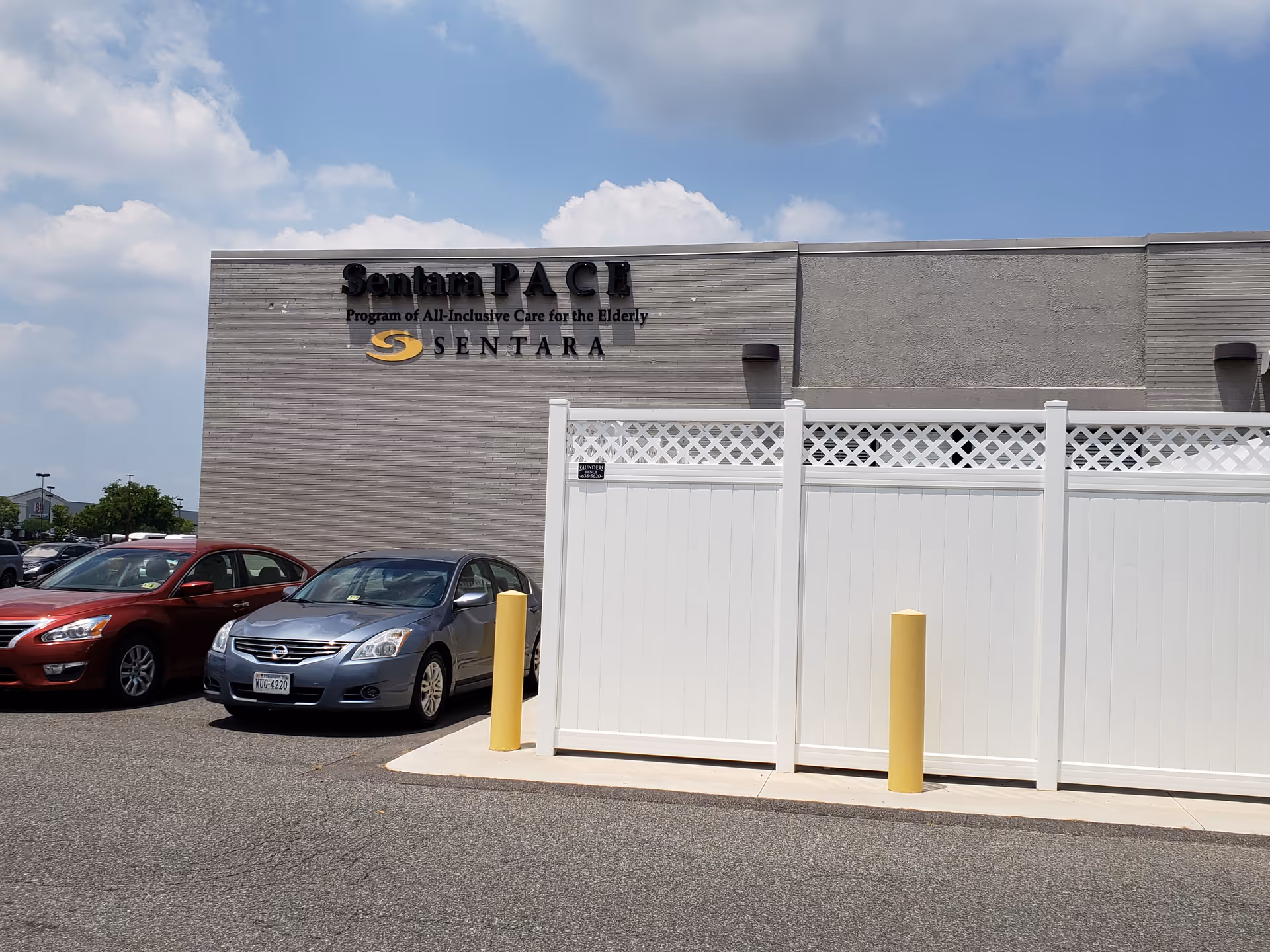 Exterior view of Sentara PACE building with a white fence and parked cars.