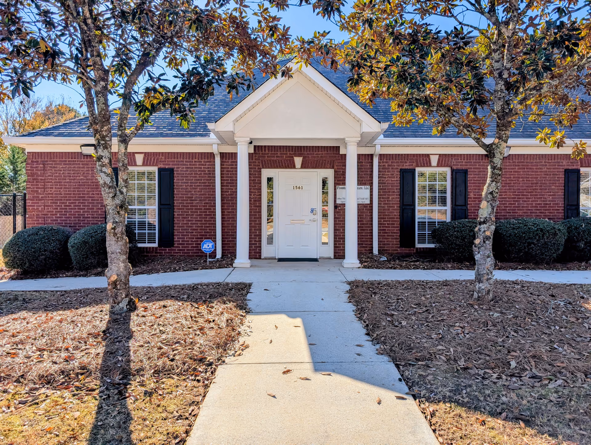 Brick senior housing facility entrance with white columns and central door, framed by trees.