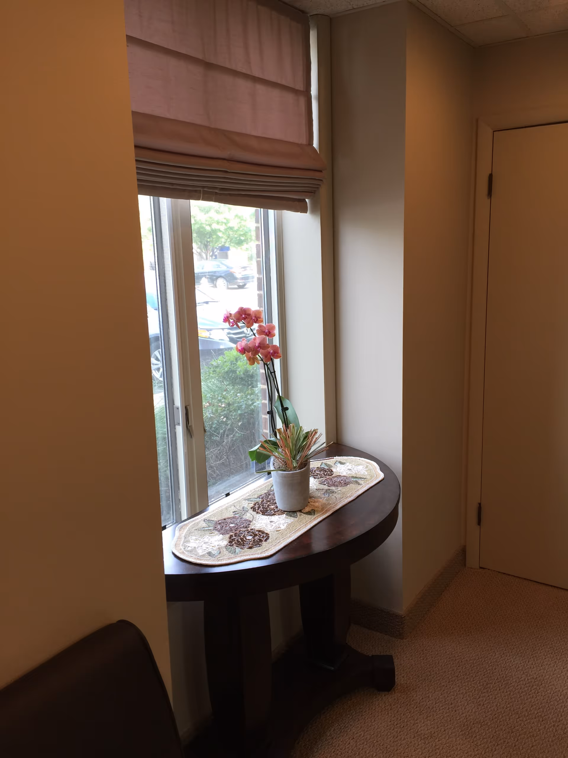 A small round wooden table by a window with a potted orchid and decorative runner
