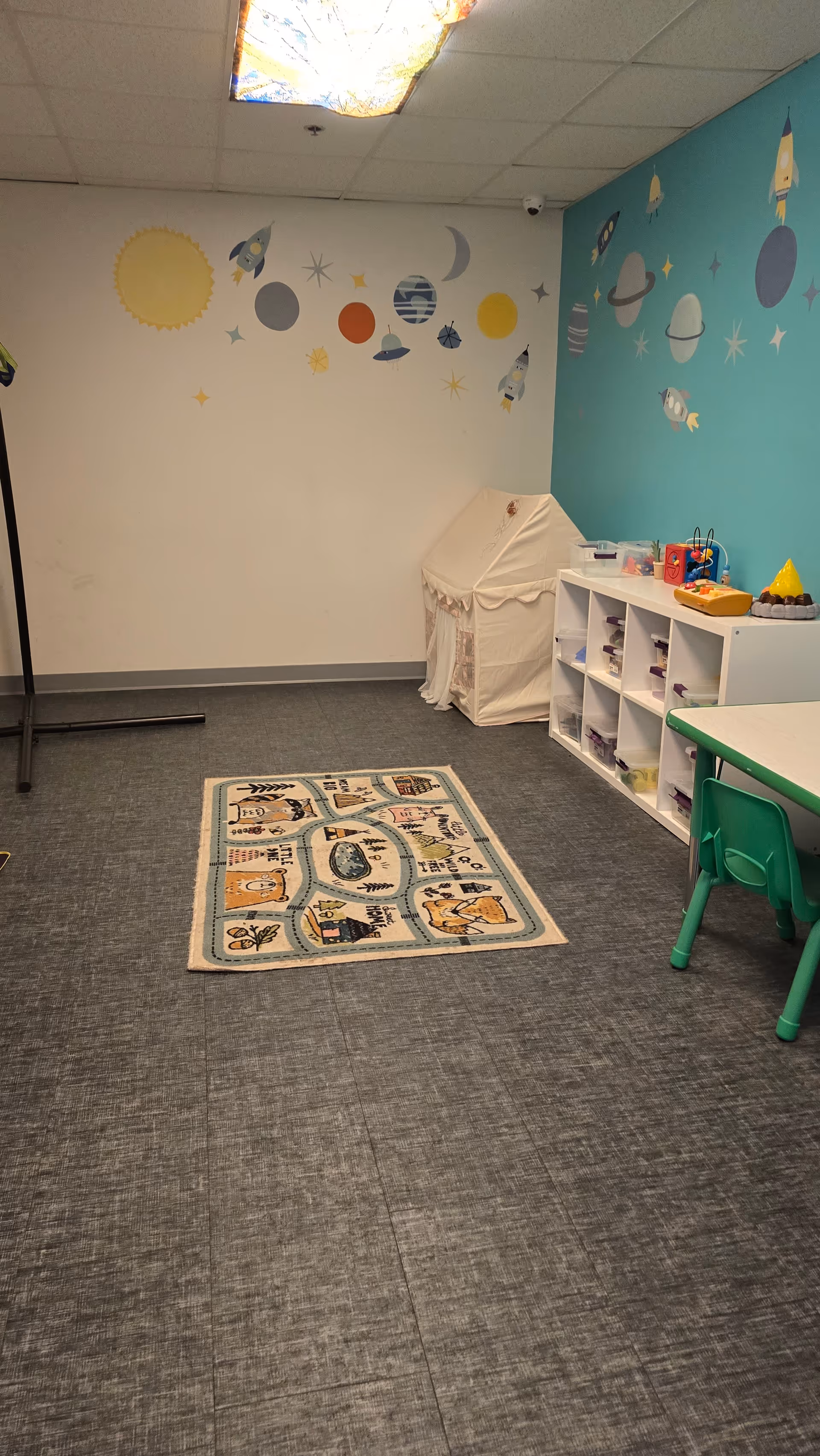 Colorful children's play room with space-themed walls, rug, tent, and cubby shelves.