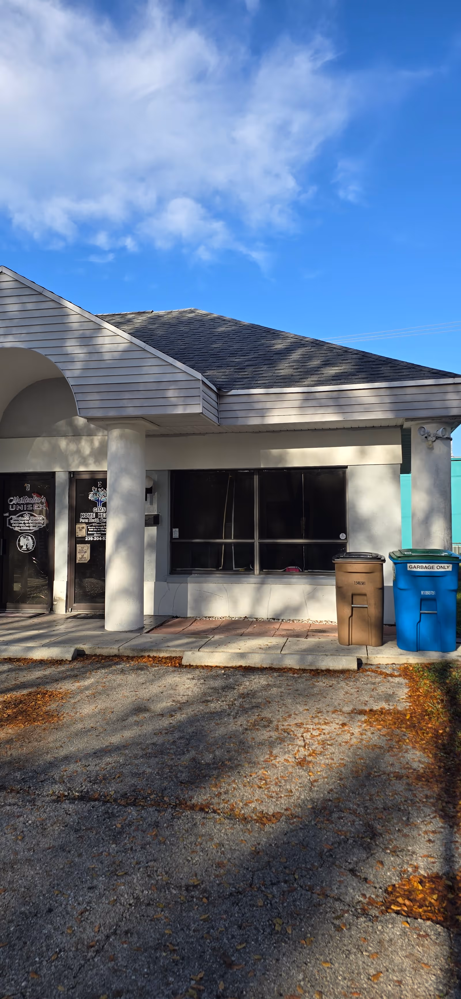 Front exterior of a single-story healthcare facility with glass windows, doors, and waste bins outside.
