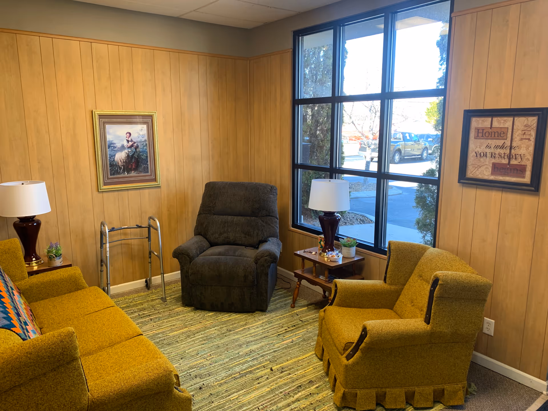 Cozy living room in a senior facility with mustard chairs, a recliner, and wood paneling.