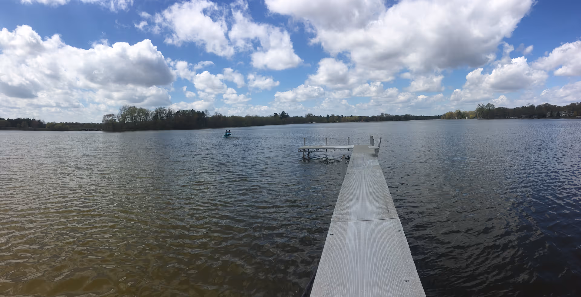 A wooden pier extends into a calm lake beneath a cloudy blue sky.