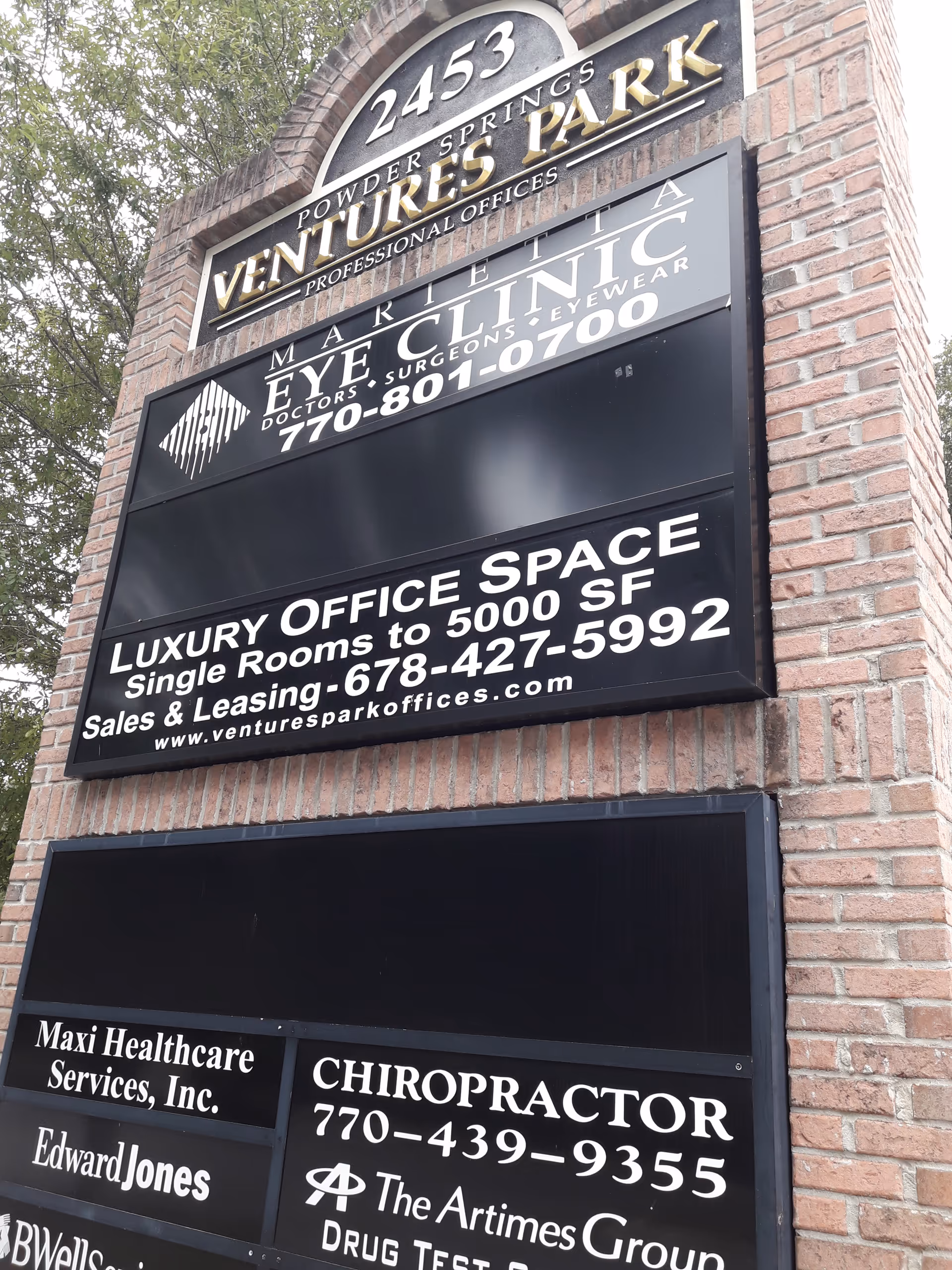 Tall brick sign structure with multiple business signs including Maxi Healthcare Services and chiropractic.